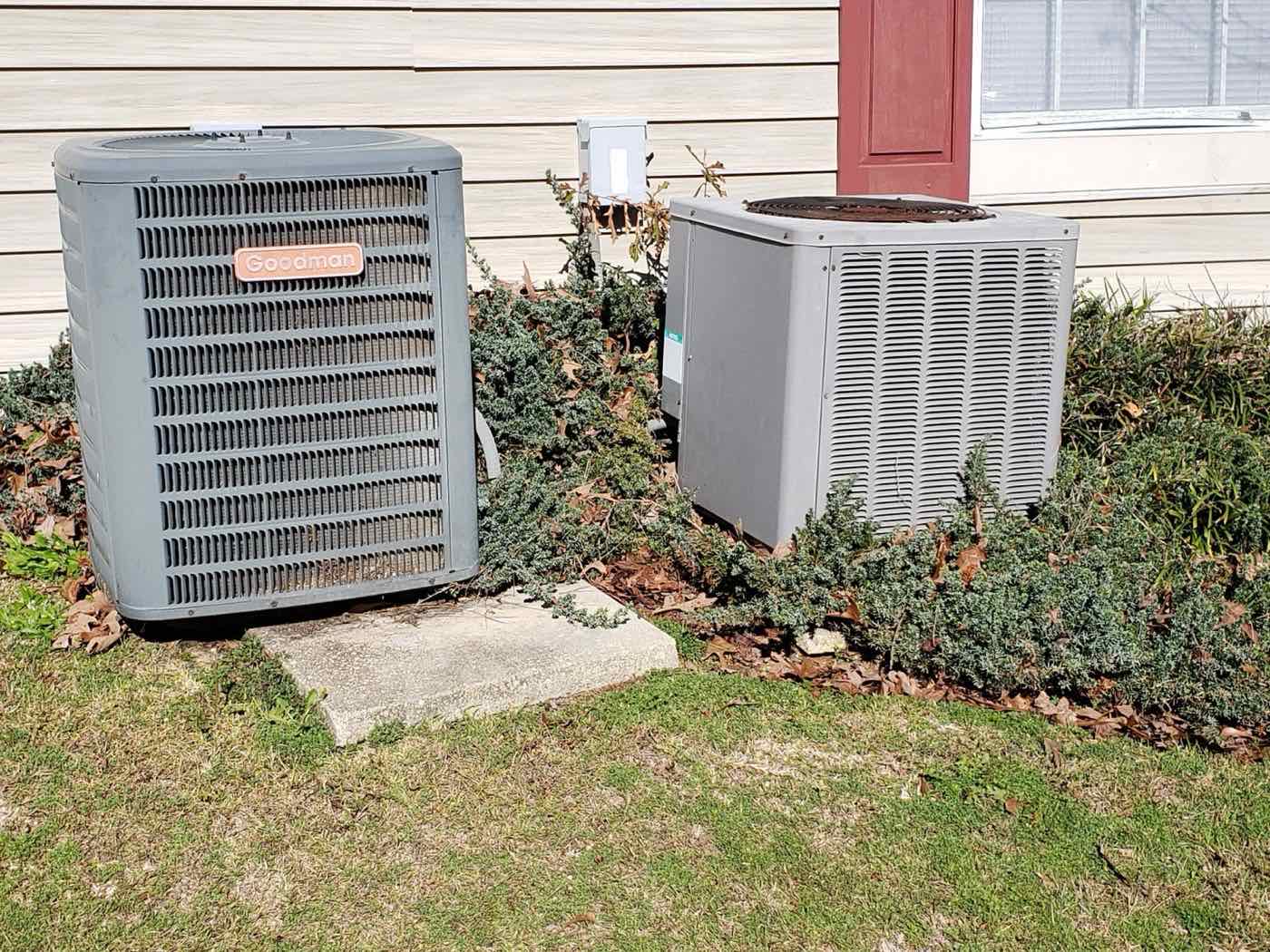 Two outdoor AC units beside a house.