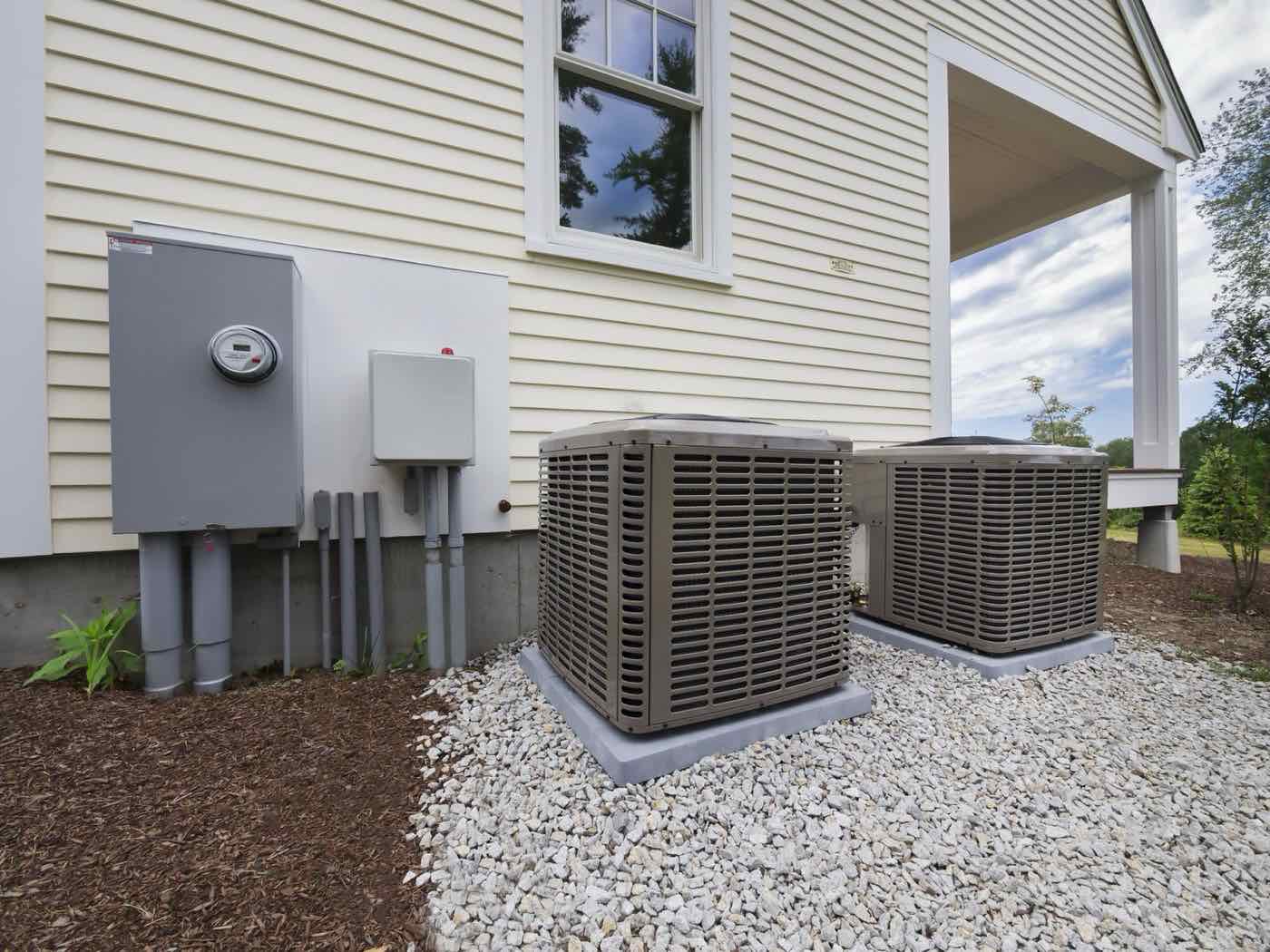 Two new outdoor AC units on a gravel pad beside a house.